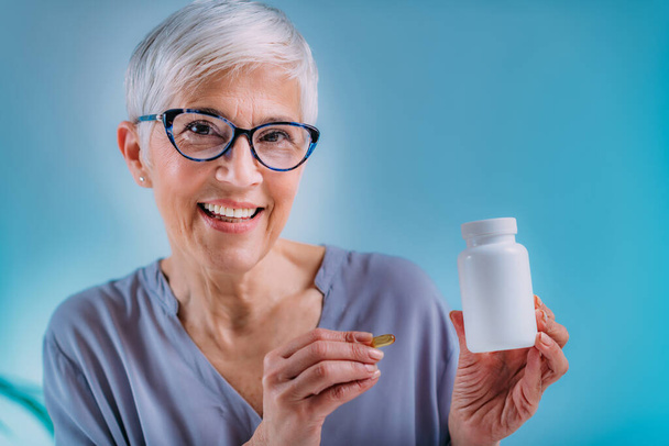 Supplementen. Senior vrouw met capsule en een blanco witte supplement container. - Foto, afbeelding