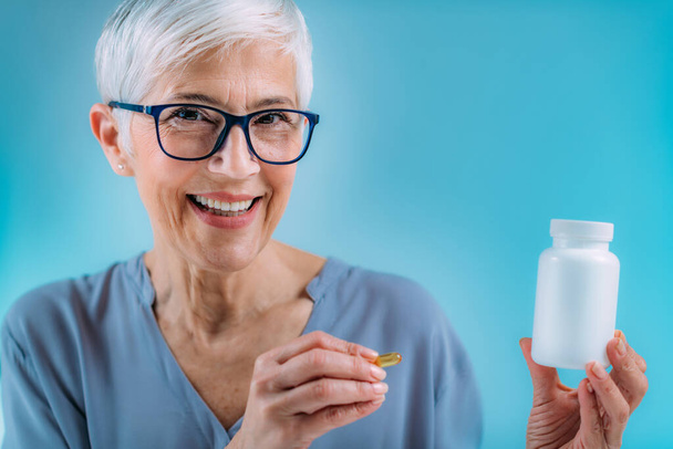 Suplementos. Mujer mayor sosteniendo cápsula y un recipiente blanco en blanco suplemento. - Foto, imagen