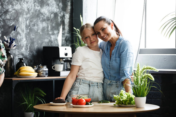 Gezond eten thuis. Gelukkige familie, moeder en dochter bereiden salade voor. vrouw en tiener meisje zijn snijden groenten in de keuken. - Foto, afbeelding