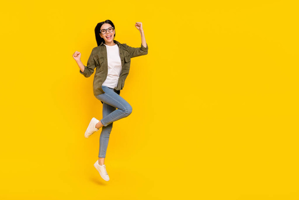 Full size photo of celebrate young lady jump wear eyewear shirt jeans sneakers isolated on yellow background - Fotoğraf, Görsel