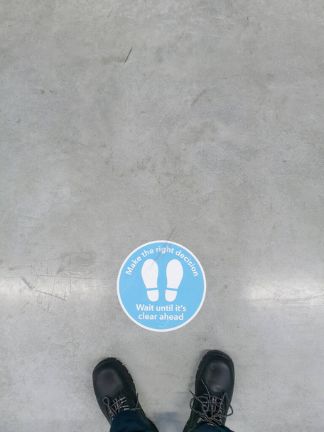 Signalisation à conseiller pour garder la distance vue sur le sol d'un entrepôt avec des bottes de sécurité devant lui. - Photo, image
