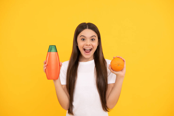 amazed teen girl long hair with body lotion and grapefruit on yellow background, cosmetic - Photo, Image
