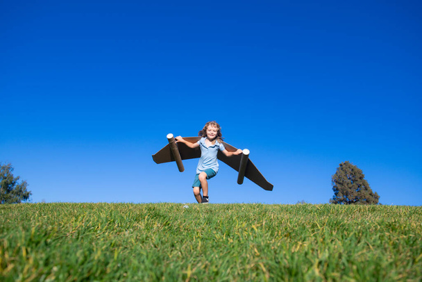 Happy child playing outside on green grass and blue sky. Kid pilot with toy jetpack. Kid boy play with toy plane cardboard. Summer travel and adventure. Success winner, imagination and dream concept. - Fotografie, Obrázek