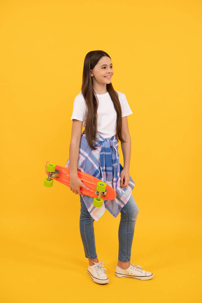 Happy kid in casual holding pennyboard yellow background, skateboarding - Photo, image