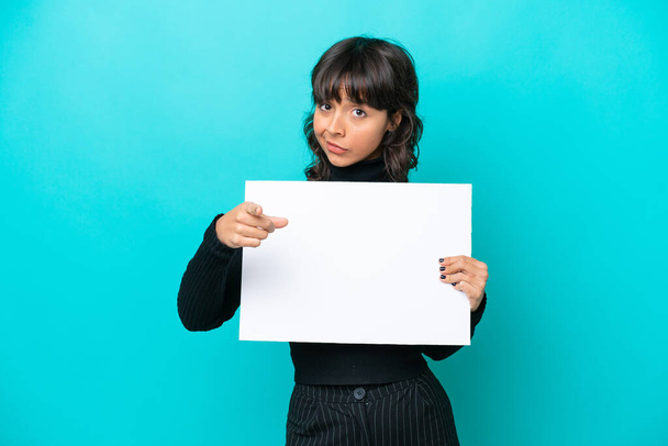 Young latin woman isolated on blue background holding an empty placard and pointing to the front - Photo, Image