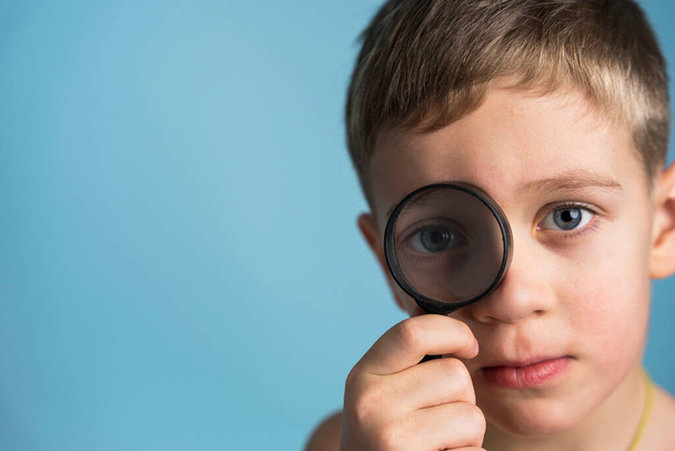 Cute Caucasian boy with a magnifying glass at the eye. funny boy looking through magnifying glass. - Zdjęcie, obraz
