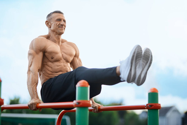 Sporty caucasian man training on parallel bars outdoors - Φωτογραφία, εικόνα