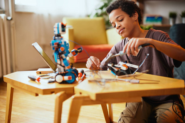 Ein afroamerikanischer Junge bastelt zu Hause einen Roboter. Ausbildung in Robotertechnik zu Hause. - Foto, Bild