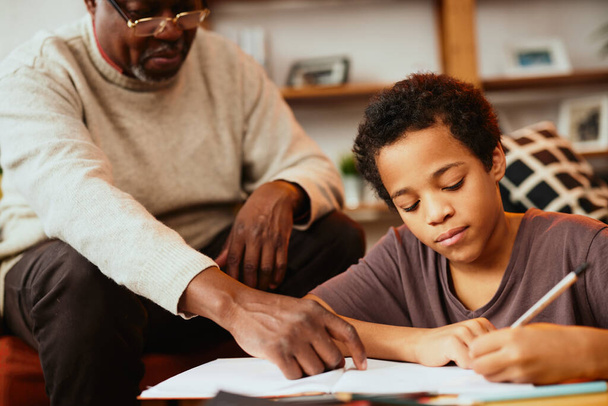 Розумний африканський хлопчик робить домашнє завдання з математики з невеликою допомогою свого дідуся. Вивчення і освіта - Фото, зображення