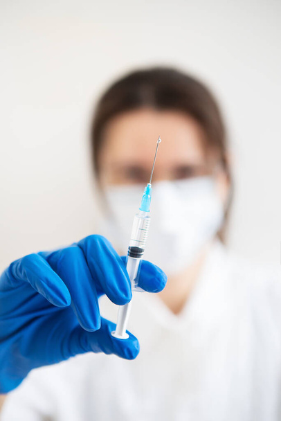 Молодой доктор со шприцем в руках. Врач в помещении делает прививку. Женщина в медицинском кабинете. Вакцинация против гриппа и вирусов - Фото, изображение