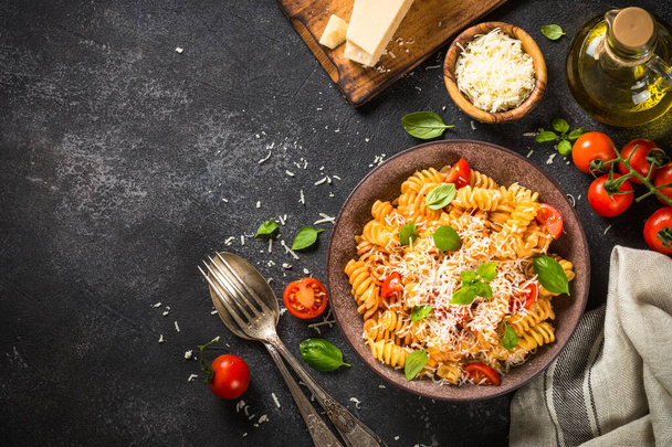 Italialainen pasta alla arrabiata basilikalla ja parmesaanijuustolla tummalla pöydällä. - Valokuva, kuva
