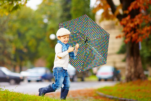 happy stylish boy with umbrella running in park - Fotó, kép