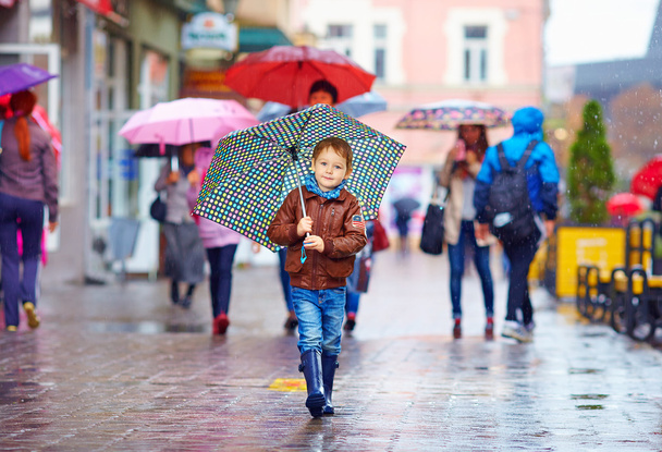 cute boy with umbrella walking on crowded city street - Fotó, kép