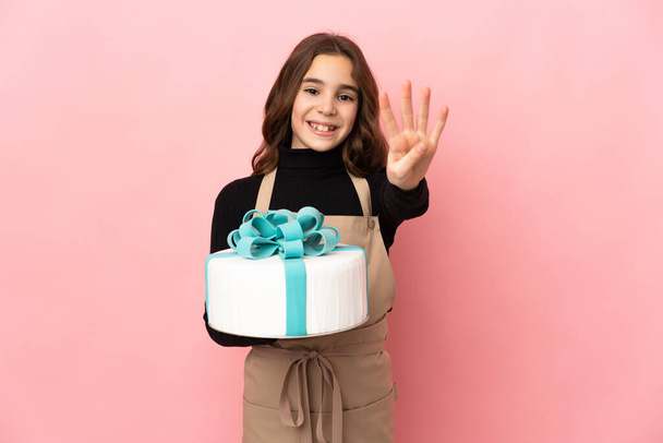 Little Pastry chef holding a big cake isolated on pink background happy and counting four with fingers - Foto, afbeelding