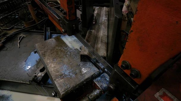 Der Meister in der Werkstatt arbeitet mit einer Bandsäge für Metall, die Maschine schneidet das Stahlprofil in beliebigem Winkel mit Seifenwasser, um das Blatt zu kühlen - Foto, Bild
