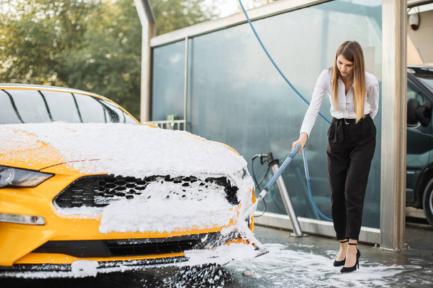 Attractive caucasian woman wear on business look washing his yellow car with foam - Zdjęcie, obraz