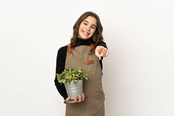 Menina segurando uma planta isolada no fundo branco apontando frente com expressão feliz - Foto, Imagem
