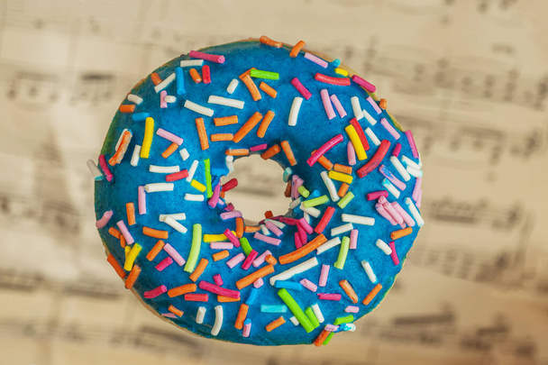 Blue glaze donut with colorful sprinkles on abstract vintage music background. Sweet food, romantic mood concept - Фото, изображение