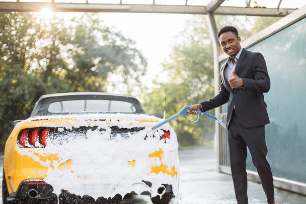 African Confident male entrepreneur cleaning his car with a jet sprayer and soap outdoors. - Fotoğraf, Görsel