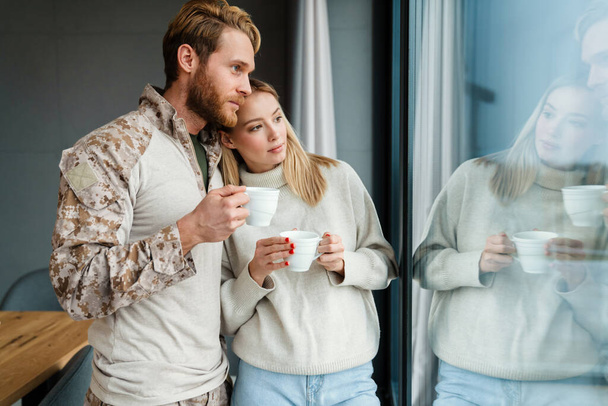 Beautiful young pleased couple drinking coffee and hugging indoors - Foto, immagini