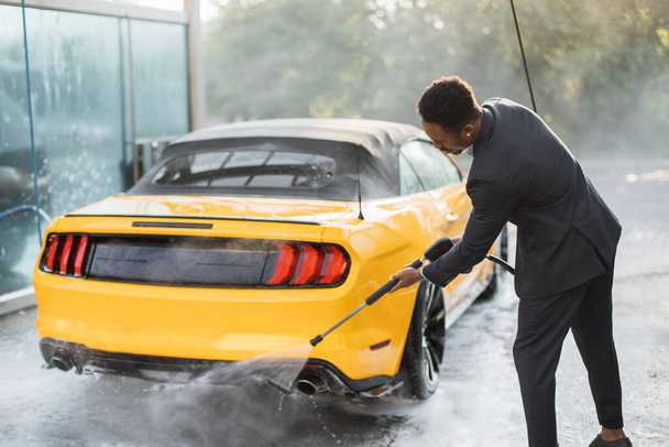 Entrepreneur in in business suit, washing back of his yellow car manually - Fotoğraf, Görsel