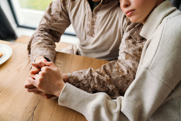 Beautiful romantic couple hugging and holding hands together while sitting at table in home - Photo, image
