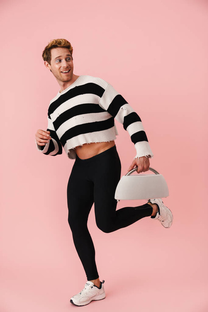 Ginger young man wearing tights smiling while holding dumbbell isolated over pink wall - Fotografie, Obrázek