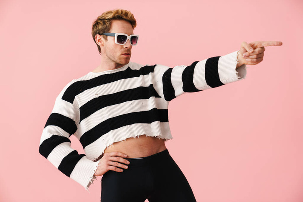 Ginger young man wearing sunglasses pointing finger aside isolated over pink wall - Φωτογραφία, εικόνα
