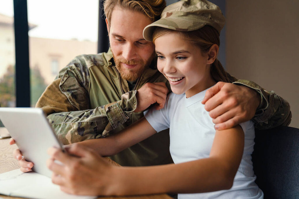 Masculine happy military man laughing and using tablet computer with her daughter at home - Fotoğraf, Görsel