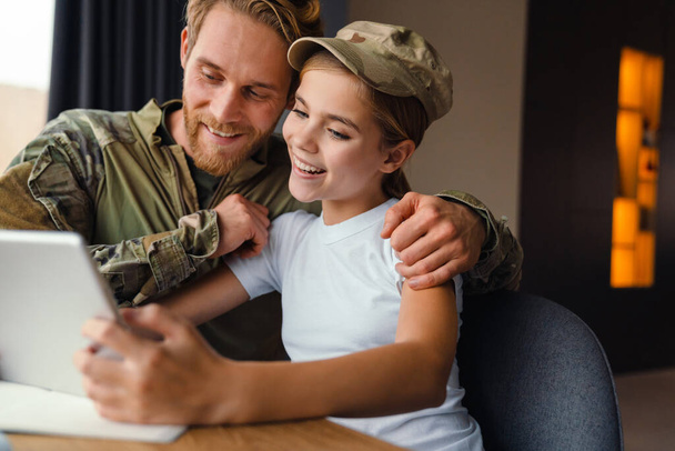 Erkeksi, mutlu bir asker kızıyla birlikte gülerek tablet bilgisayar kullanıyor. - Fotoğraf, Görsel