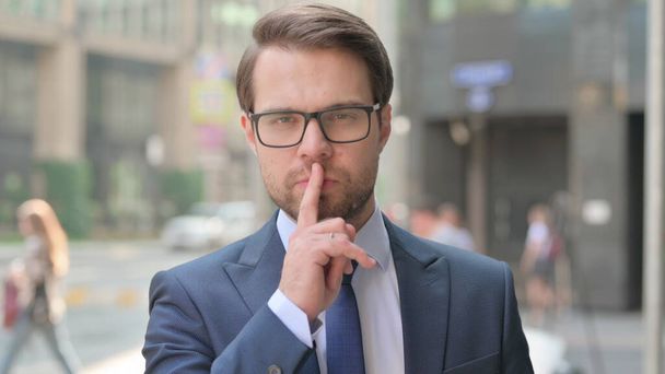Outdoor Attractive Young Businessman Putting Finger on Lips - Fotó, kép
