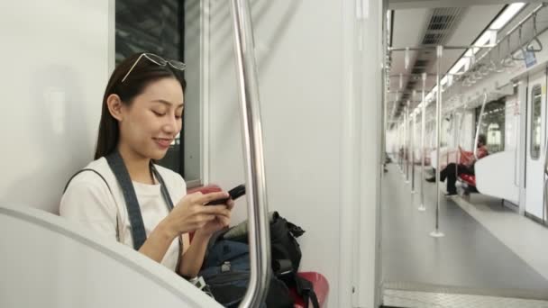 Hermosa turista asiática con cámara se sienta en el tren del cielo, el mensaje de chat de teléfono móvil, el transporte de viajes en una estación de tren, el estilo de vida de los pasajeros de la ciudad, feliz viaje de vacaciones en Tailandia. - Metraje, vídeo