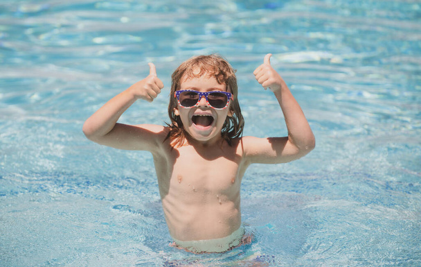 Child in summer swimming pool. Cute child boy with thumbs up swim in swimming pool, summer water background with copy space. Funny kids face. Thumbs up. - Фото, изображение