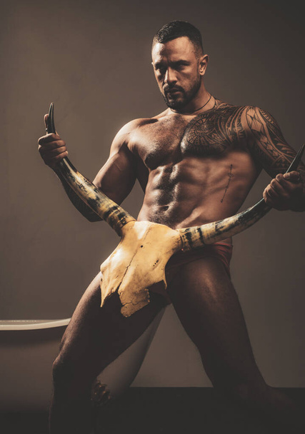 Strong sexy nude man with bull skull on grey background. - Photo, Image