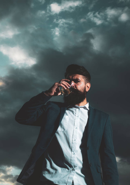 Man with beard and mustache holds alcoholic beverage on sky background. Service and alcoholism concept. - Fotoğraf, Görsel