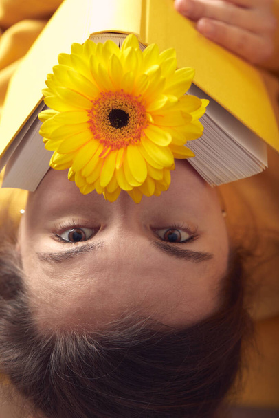 Portrait of a beautiful girl with a yellow book and a gerbera flower. - Photo, image