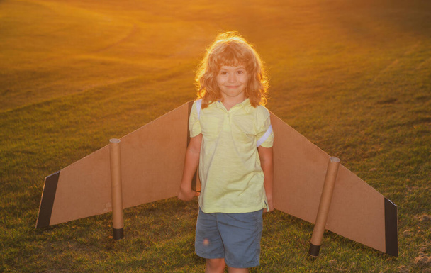 Kid traveller with backpack wings at sunset grass field. Child playing pilot aviator and dreams outdoors in park. - Fotó, kép