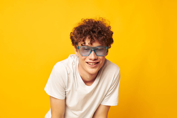 portrait of a young curly man in a white t-shirt blue fashion glasses isolated background unaltered - Foto, afbeelding