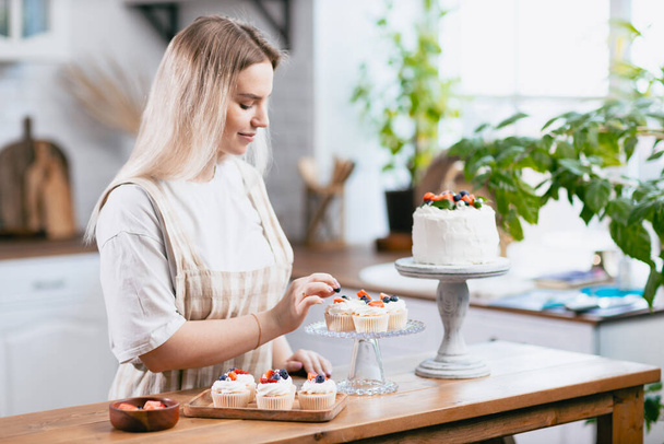 Ζαχαροπλαστείο σεφ ζαχαροπλάστης νεαρή καυκάσια γυναίκα με κέικ στο τραπέζι της κουζίνας. - Φωτογραφία, εικόνα
