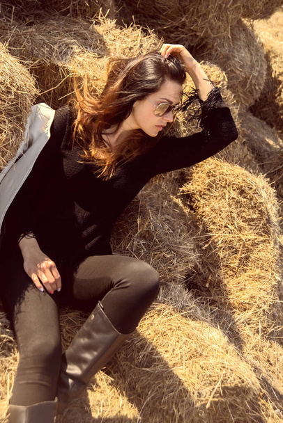  girl in a black stylish clothes and leather high boots posing on straw - Foto, immagini
