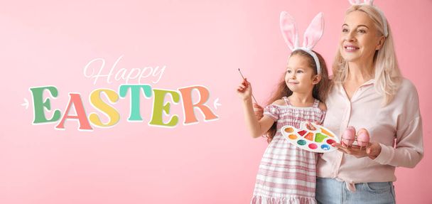 Mutlu küçük kız ve büyükannesi Paskalya yumurtaları ve pembe arka planda boyalarıyla - Fotoğraf, Görsel