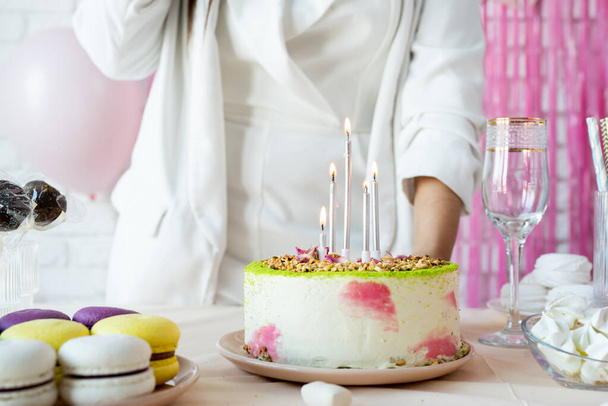 Fiesta de cumpleaños. Mesas de cumpleaños. Mujer atractiva en ropa de fiesta blanca preparando mesa de cumpleaños con pasteles, pastelitos, macarrones y otros dulces, encendiendo las velas - Foto, Imagen