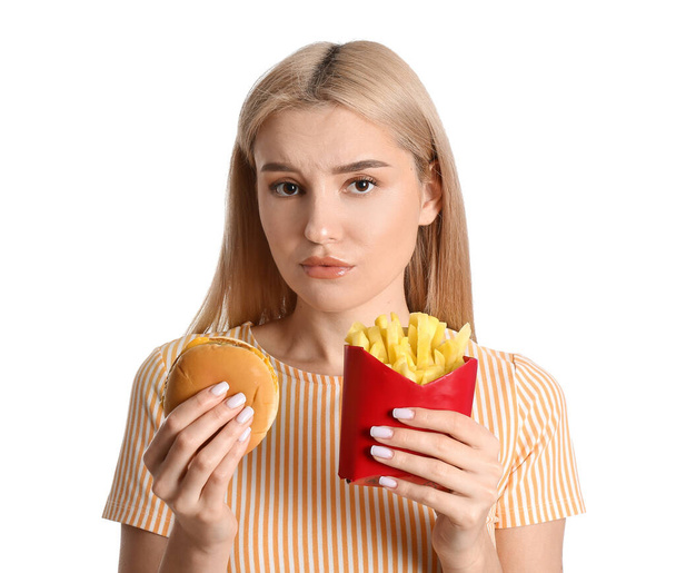 Напряженная молодая женщина с картошкой фри и бургером на белом фоне - Фото, изображение