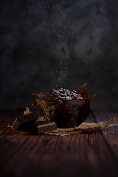 Muffin de chocolate com açúcar em pó em cima em um fundo de madeira escura. - Foto, Imagem