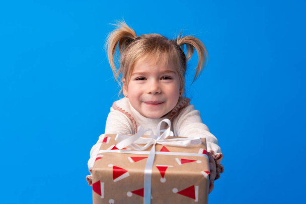 Happy little girl holding agift box on a blue background - Фото, изображение