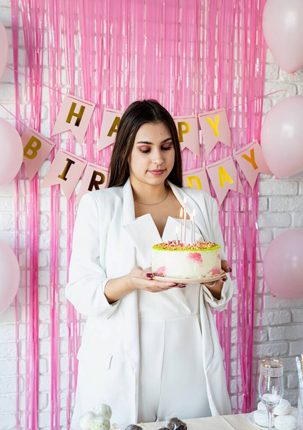 Doğum günü partisi. Doğum günü masaları. Beyaz parti kıyafetleri içinde çekici bir kadın doğum günü masasını kek, pasta, badem kurabiyesi ve diğer şekerlerle hazırlıyor. - Fotoğraf, Görsel