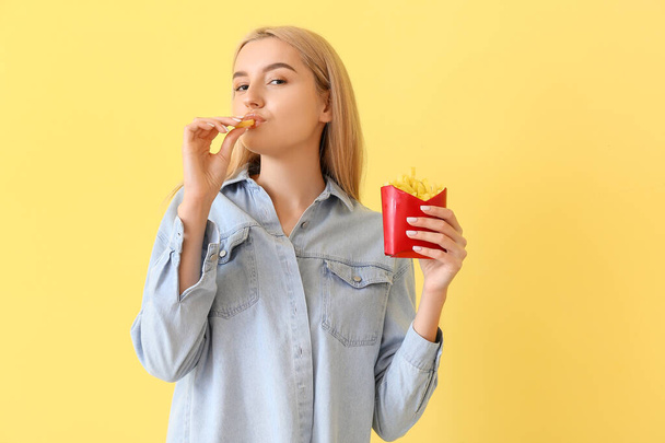 Young woman eating french fries on yellow background - Фото, зображення