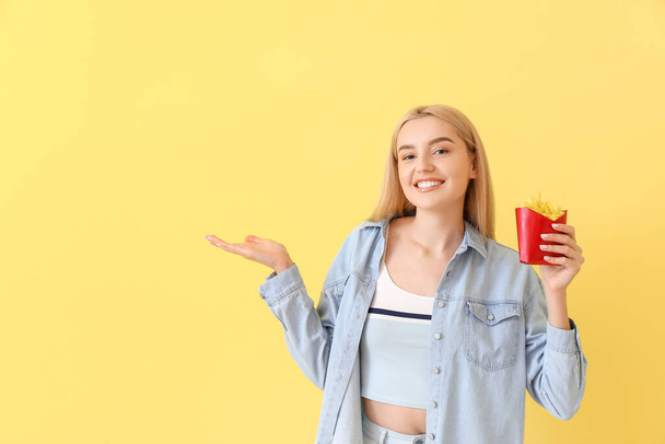 Счастливая молодая женщина с картошкой фри показывает что-то на желтом фоне - Фото, изображение