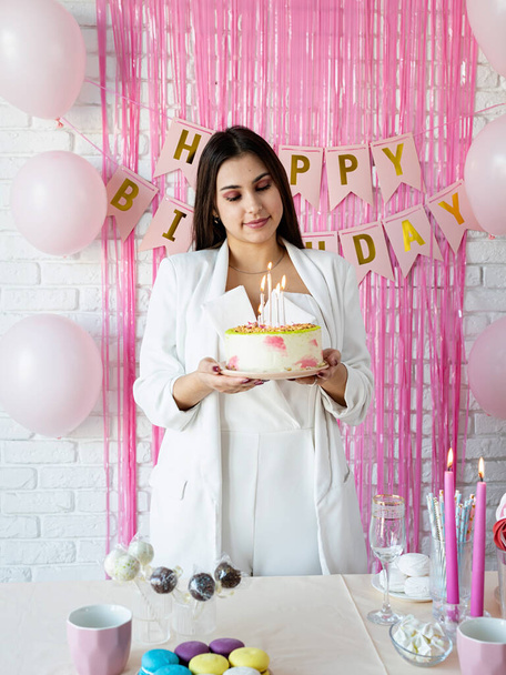 Festa de aniversário. Mesas de aniversário. Mulher atraente em roupas brancas da festa preparando mesa de aniversário com bolos, bolos, macarons e outros doces - Foto, Imagem