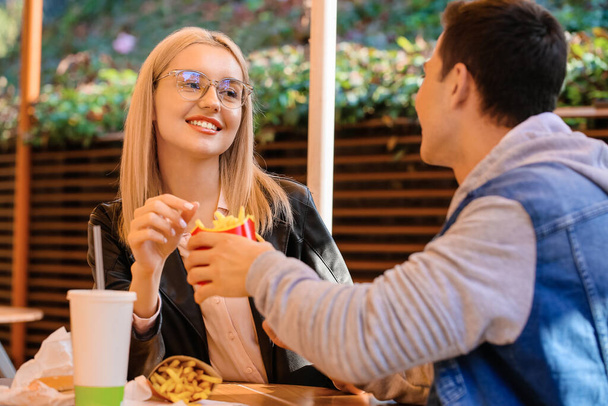 Pareja joven comiendo papas fritas en la cafetería al aire libre - Foto, imagen